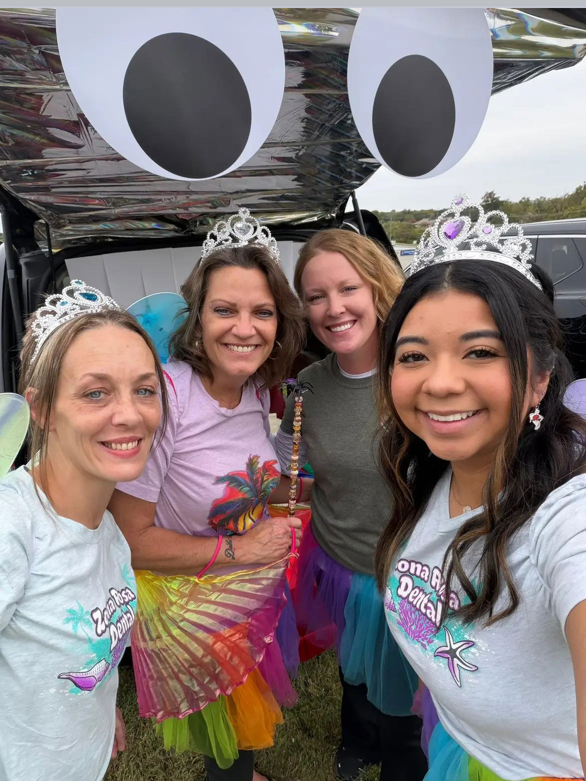 The image shows four individuals posing with a large inflatable balloon decoration featuring a cartoon face.