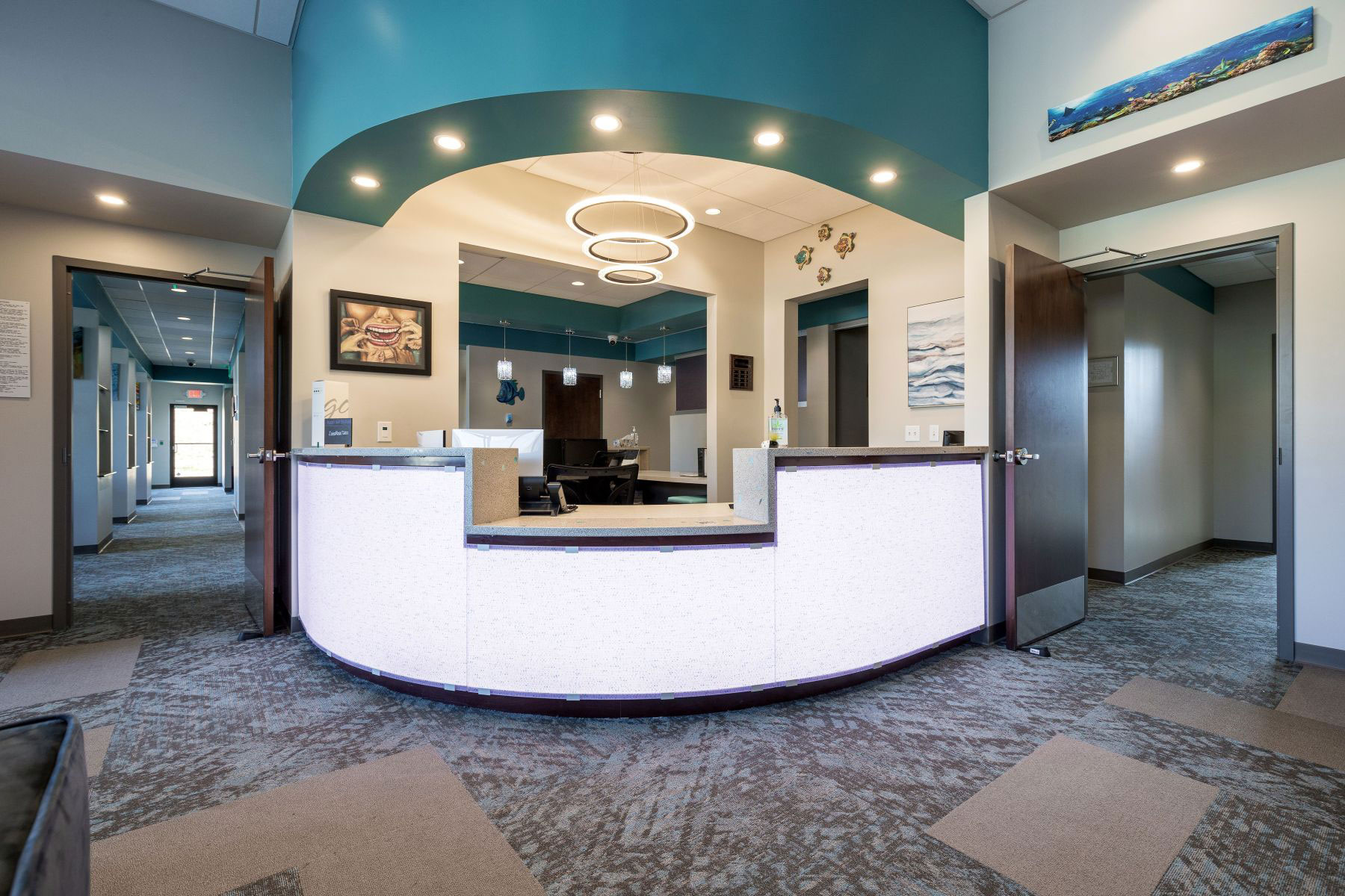 The image shows an interior view of a lobby with a curved counter featuring a reception area, a modern design with a color scheme of blue and white, and a sign with a photo of a person.