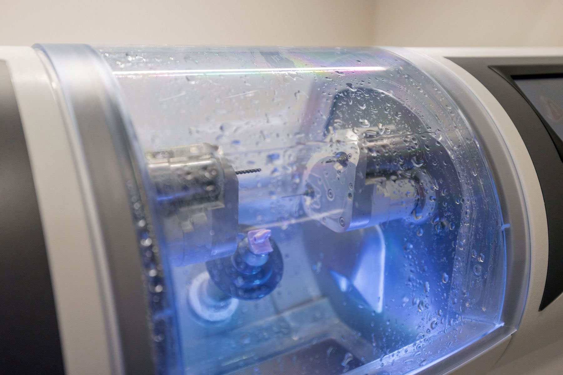 The image shows a close-up of an industrial or scientific machine with various components, including a blue illuminated area at the bottom, which appears to be a part of a larger device possibly related to medical or research equipment.