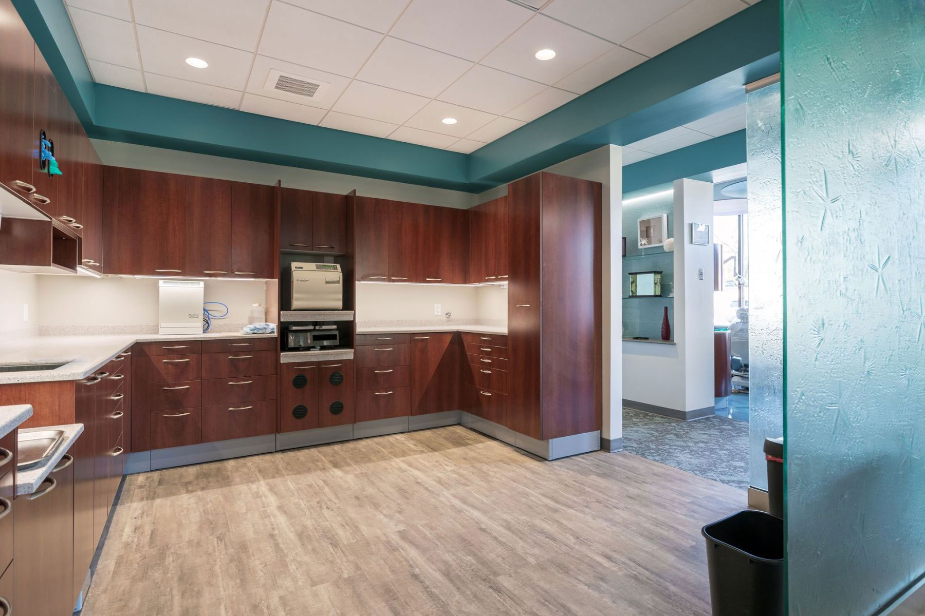 The image depicts an interior view of a modern office space with sleek furniture, including wooden cabinets, a countertop, and a kitchen area with appliances such as a microwave and sink.