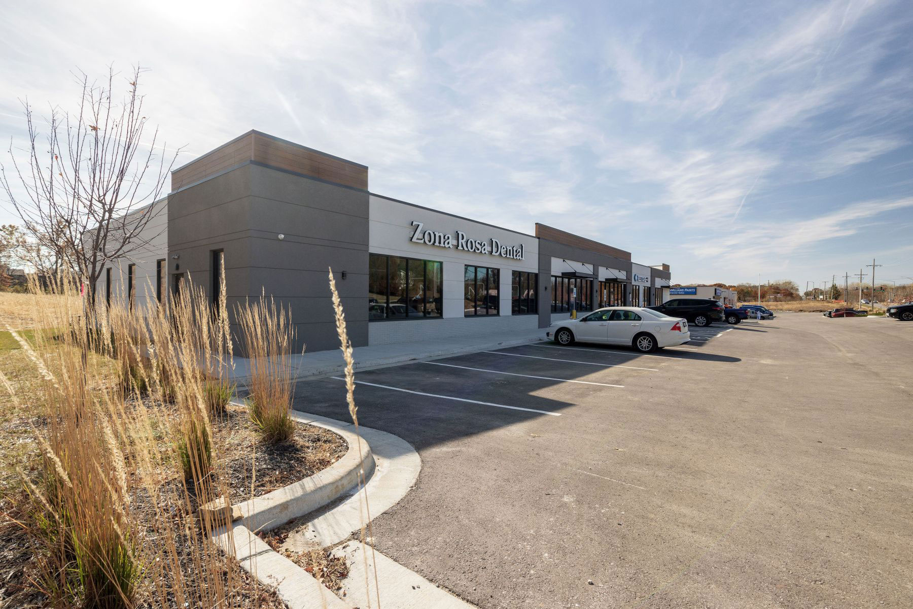 The image depicts a modern building with a sign that reads Z s Blue Lounge on its exterior, surrounded by a parking lot with several vehicles parked and a clear sky above.